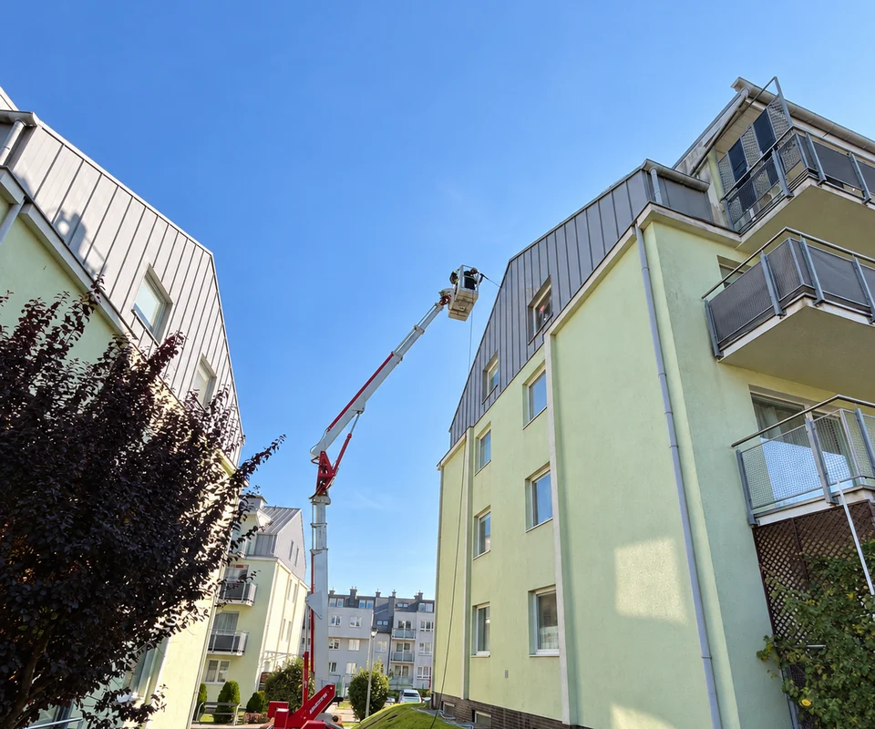 Pracownik SoftWash24 na podnośniku podczas mycia elewacji budynku mieszkalnego.